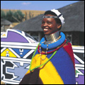 Ndebele woman wearing traditional neck rings and jewellery outside a decorated homestead